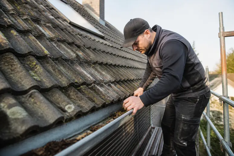Artisan couvreur inspectant les tuiles et nettoyant les gouttières lors d'une visite d'entretien de toiture