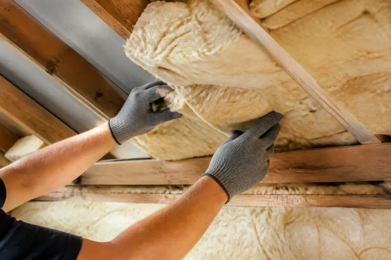 Mains plaçant l'isolant entre les chevrons pour une isolation toiture par l'intérieur