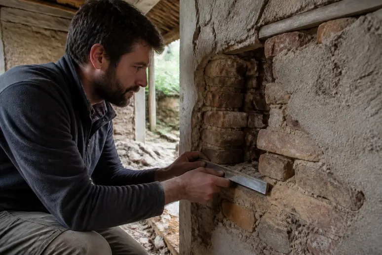 Artisan examinant l'état d'un mur dégradé avant la rénovation d'une maison ancienne dans l'Aisne.