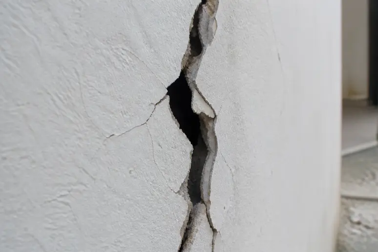 Gros plan sur une fissure profonde et traversante dans un mur intérieur de maison.