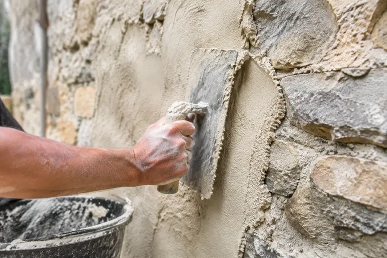 Application d'un enduit à la chaux sur un mur ancien en pierre pour éviter l'humidité.