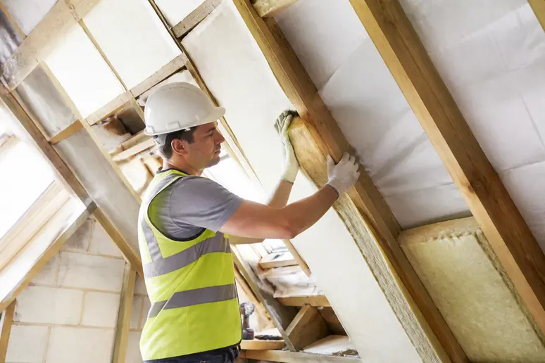 Artisan posant de l'isolant thermique sous les rampants de toiture lors de travaux d'isolation sous toiture