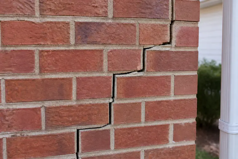 Fissure en escalier suivant les joints de maçonnerie sur le mur extérieur d'une maison fissurée