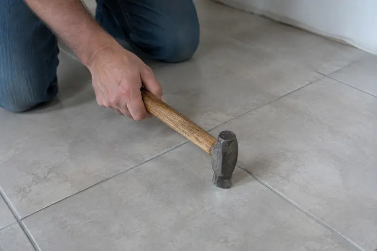 Artisan tapotant un ancien carrelage avec le manche d'un outil pour repérer les zones creuses avant la pose.