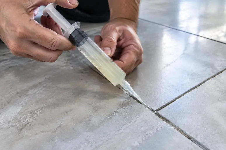Injection de résine époxy à la seringue dans un joint pour réparer un carreau creux.