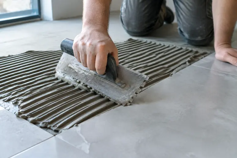 Application minutieuse de colle pour le double encollage de grands carreaux de carrelage.