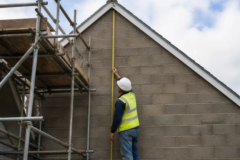 Ouvrier mesurant la surface d'un mur pignon depuis un échafaudage pour estimer le prix de rénovation au mètre carré