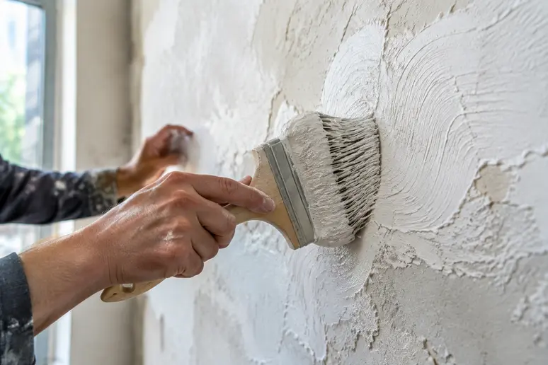 Application d'un enduit décoratif à la brosse sur un mur intérieur irrégulier.