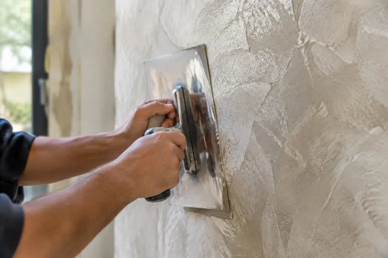 Lissage d'un enduit décoratif à la taloche inox sur une surface murale.