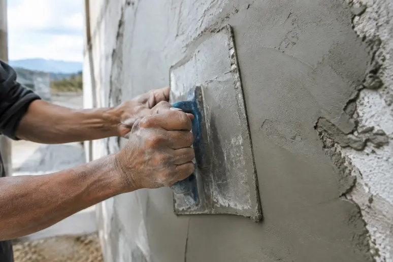 Mains utilisant une lame à lisser pour répartir l'enduit sur un mur irrégulier